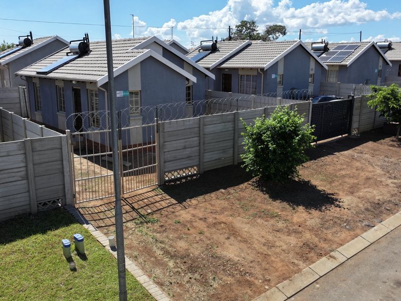 Aerial view of a residential complex featuring multiple detached houses with tiled roofs, solar geysers, and secure precast concrete boundary walls with razor wire.