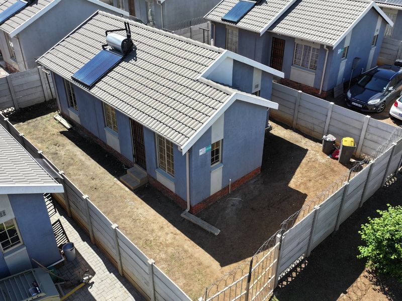 Aerial view of a detached residential property featuring a tiled roof with a solar water heater, enclosed by precast concrete walls with security fencing.