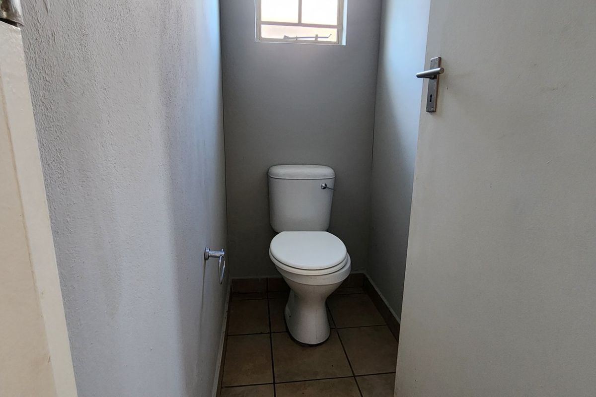 A compact, functional guest toilet featuring tiled flooring and a small window, presenting a blank canvas for potential cosmetic updates.
