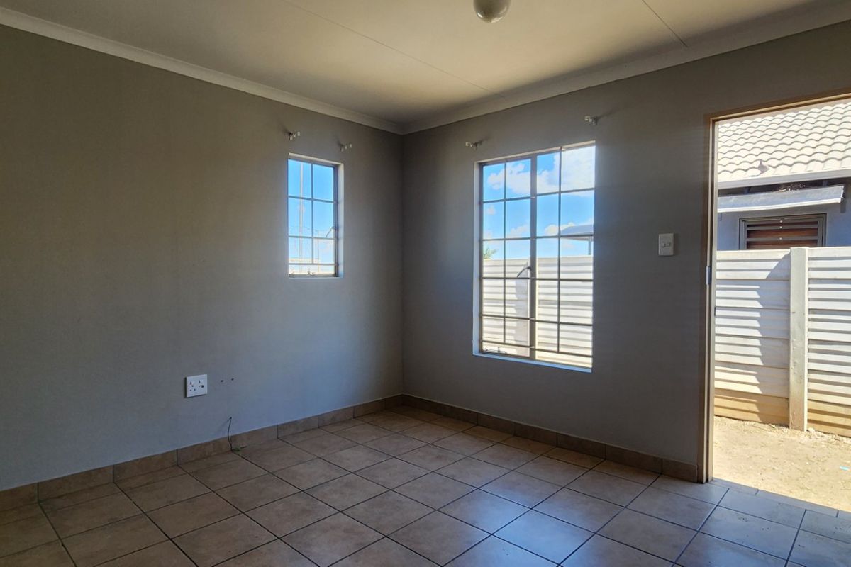 A clean, empty bedroom featuring neutral wall tones, tiled flooring, and natural light through grid-pattern windows with direct access to the exterior.