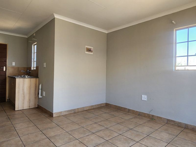 An open-plan living area featuring tiled flooring, neutral walls, and a compact kitchenette with built-in cabinetry and a hob.