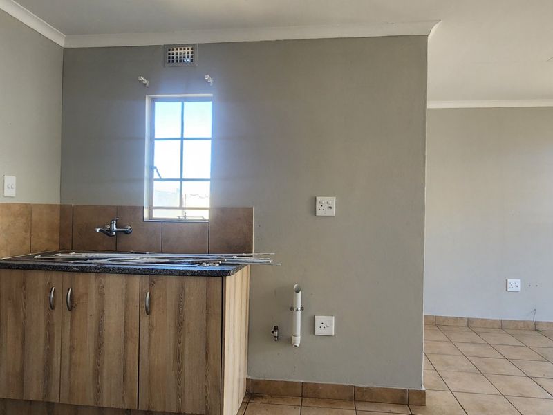 An open-plan living area featuring tiled floors and a basic kitchen sink unit with cabinetry. The space is currently vacant and requires finishing.