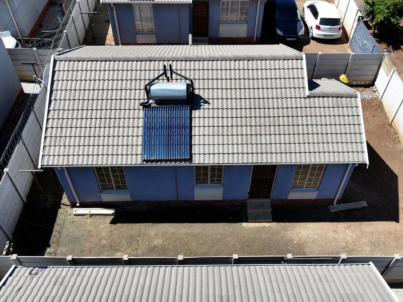Aerial view of a residential property featuring a tiled roof with an installed solar water heating system and a secure perimeter boundary wall.