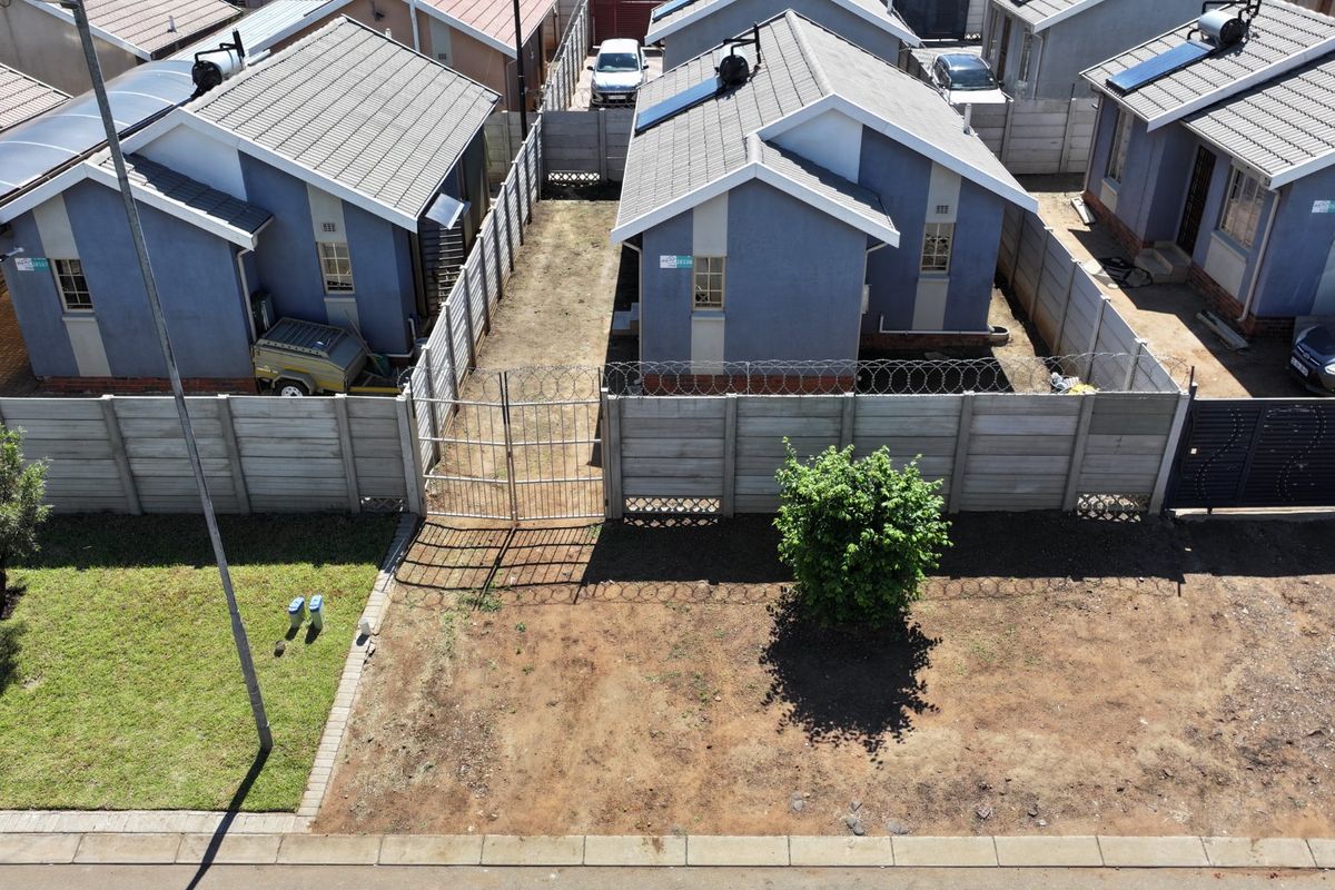 Aerial view of a residential property featuring tiled roof houses with solar geysers, enclosed by precast concrete boundary walls with security razor wire.