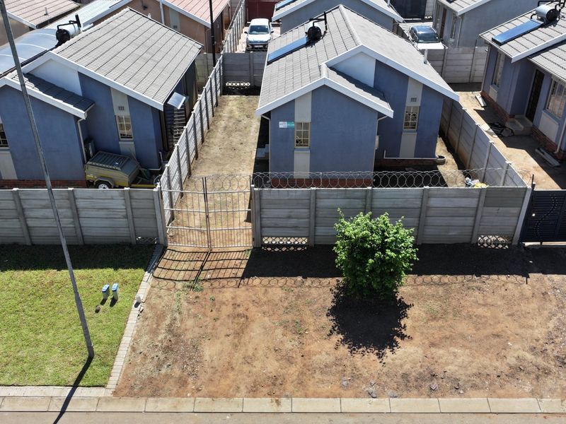 Aerial view of a residential property featuring tiled roof houses with solar geysers, enclosed by precast concrete boundary walls with security razor wire.