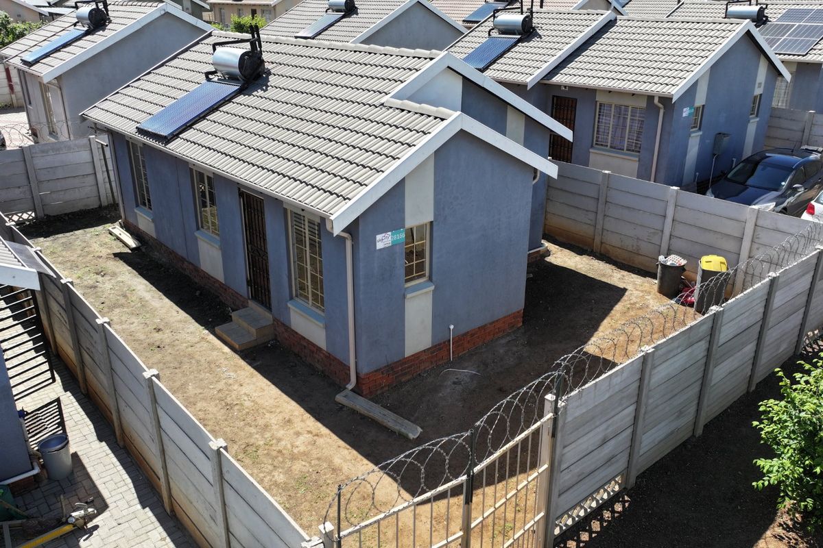 Aerial view of a residential property featuring a tiled roof with a solar water heater, enclosed by a precast concrete wall with security fencing.