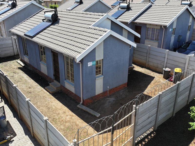 Aerial view of a residential property featuring a tiled roof with a solar water heater, enclosed by a precast concrete wall with security fencing.
