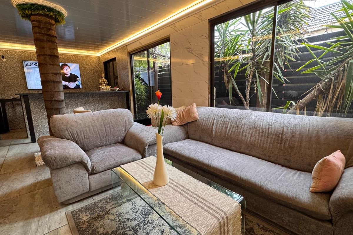 Modern living room featuring marble-effect wall cladding, recessed LED lighting, tiled floors, and a built-in bar area with large sliding doors to the garden.