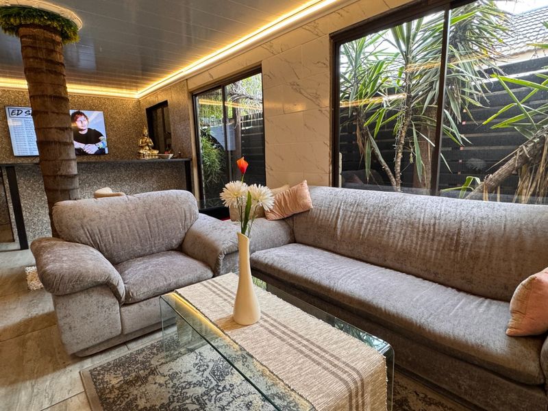 Modern living room featuring marble-effect wall cladding, recessed LED lighting, tiled floors, and a built-in bar area with large sliding doors to the garden.