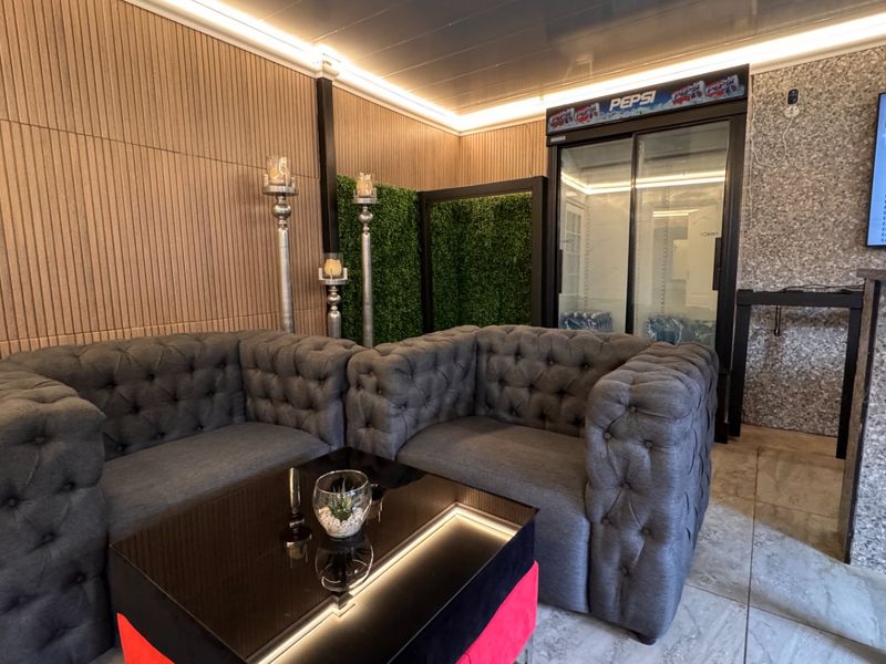 A modern entertainment bar area featuring slatted timber wall paneling, recessed LED lighting, a built-in glass display fridge, and contemporary stone-look wall finishes.