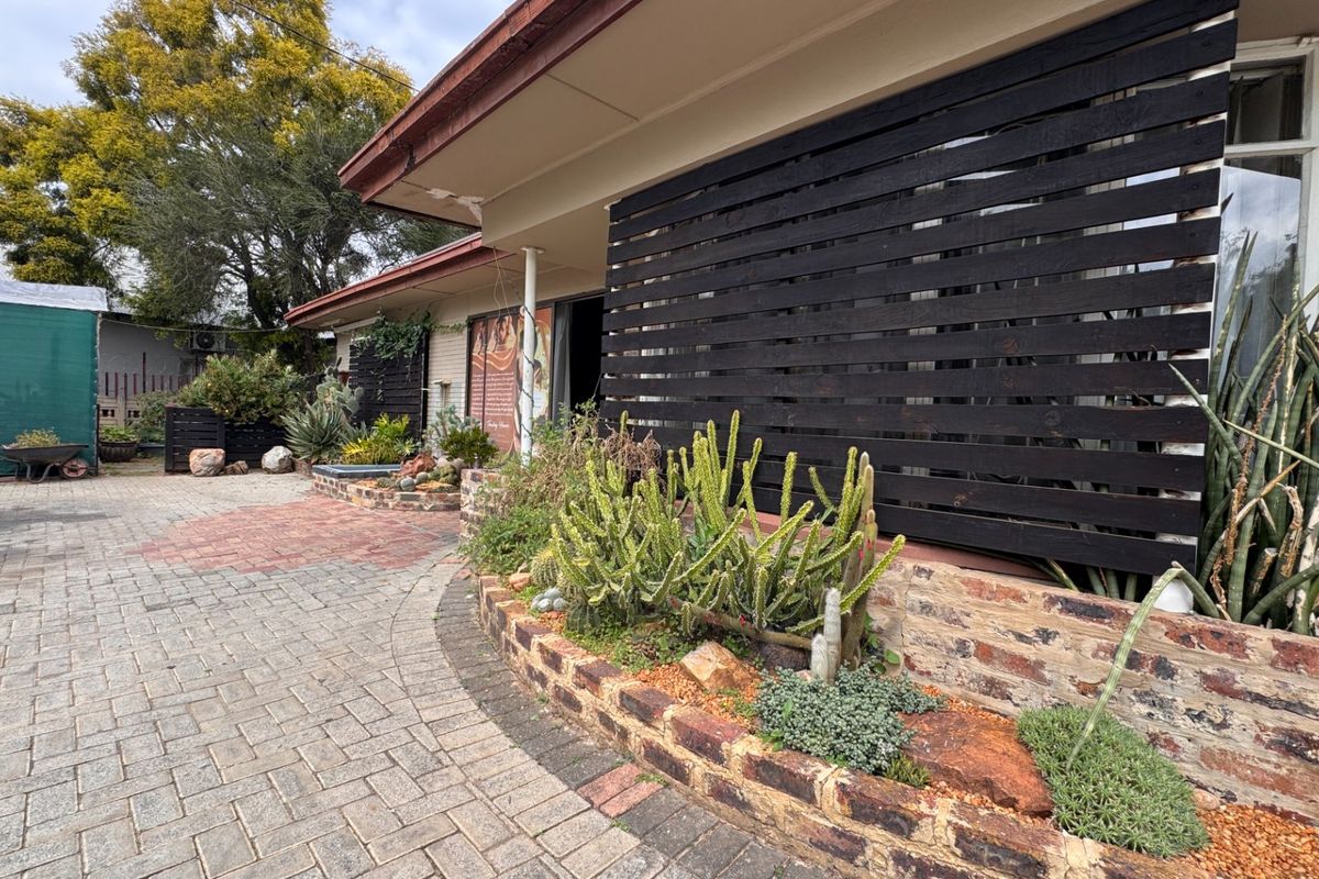 Rear exterior view featuring a brick paved courtyard, raised garden beds, and a timber privacy screen attached to the home's covered patio area.