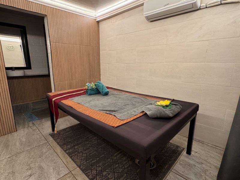 A compact room featuring modern slatted wood wall paneling, tiled flooring, and a wall-mounted air conditioning unit, with an adjacent small wash area.