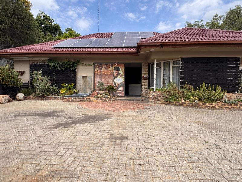 Front elevation of a single-story house featuring a tiled roof with solar panels, a brick-paved driveway, and a landscaped entrance with a water feature.