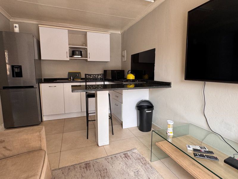 Compact open-plan living area featuring a functional kitchen with built-in cabinetry, granite countertops, and tiled flooring, seamlessly integrated with the lounge space.