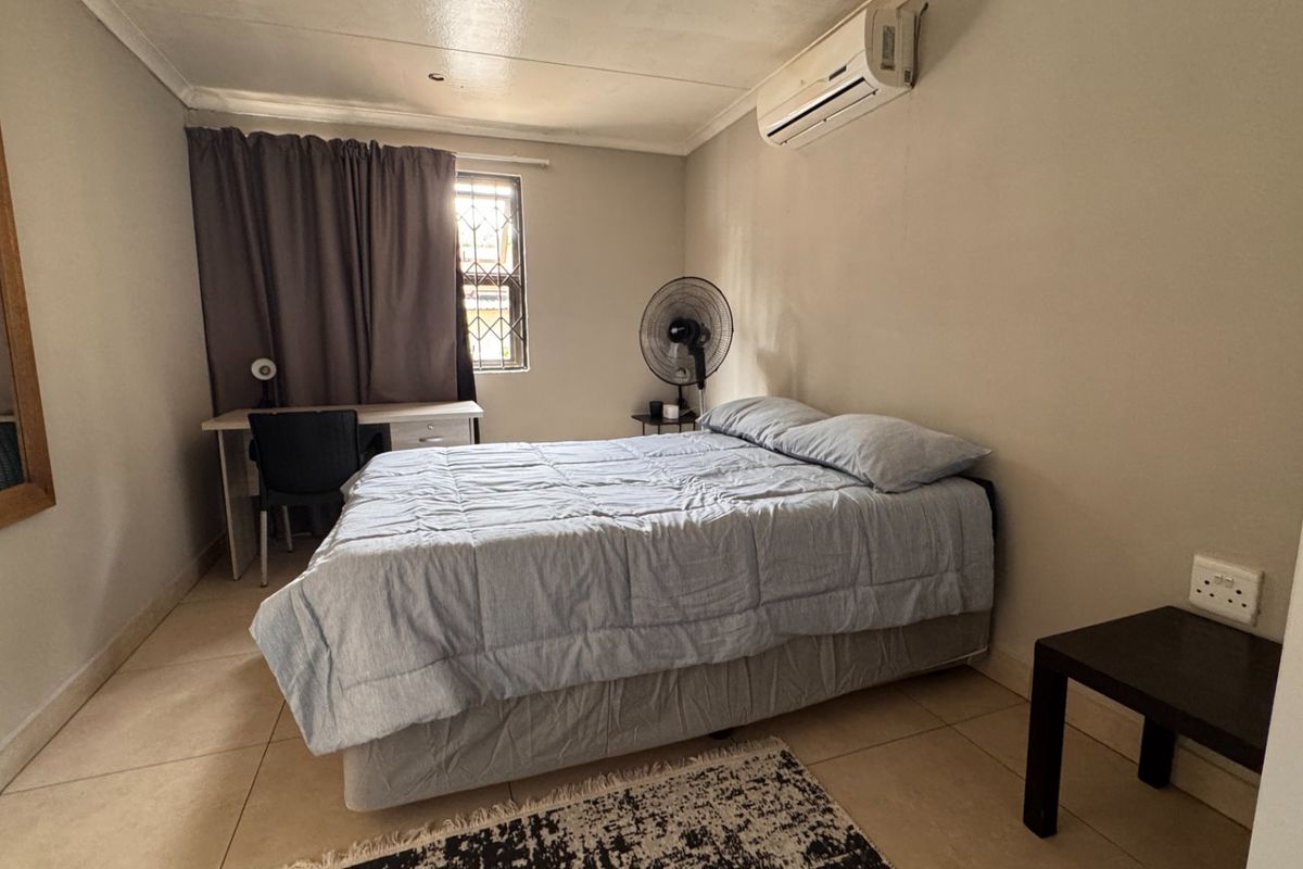 A functional bedroom featuring tiled flooring, an integrated air conditioning unit, and a window with security bars.