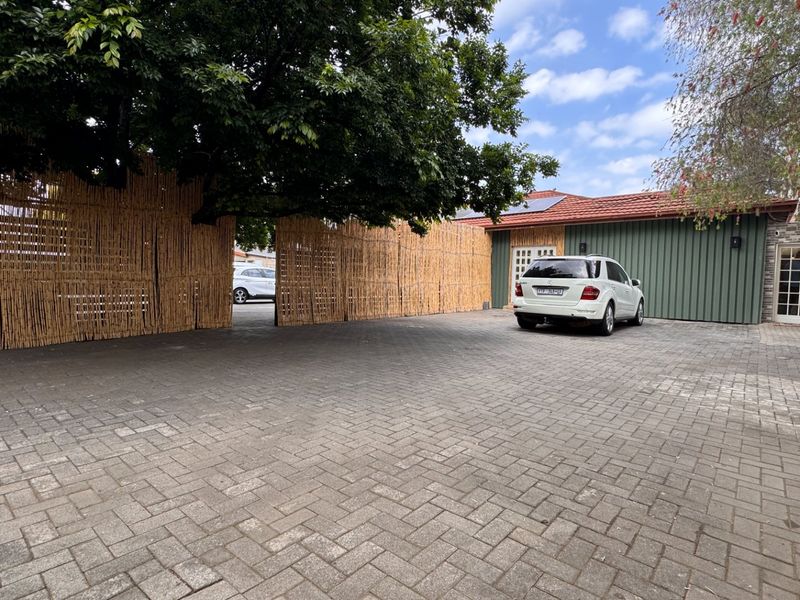 A spacious paved driveway area featuring a bamboo privacy screen, solar panels on the roof, and direct access to the property entrance.