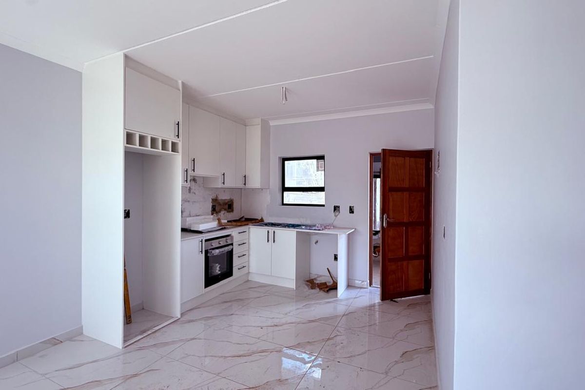 A partially completed kitchen featuring white cabinetry, an integrated oven, and marble-look floor tiles, currently awaiting final finishes and sink installation.
