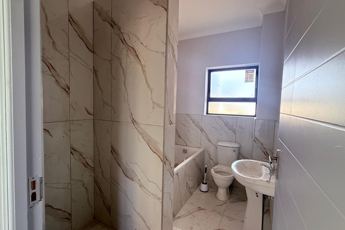 A modern bathroom featuring marble-look wall and floor tiles, a pedestal sink, toilet, and a bathtub, currently awaiting final finishing touches.