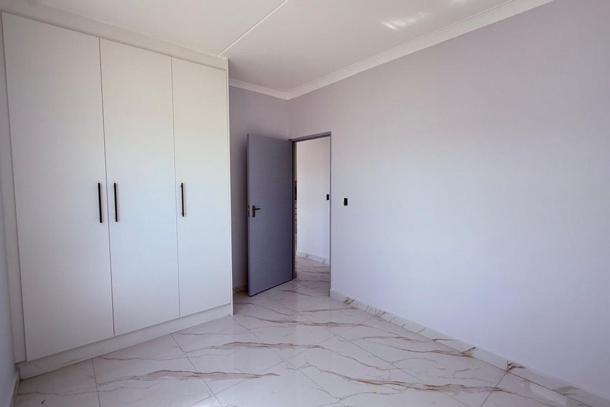 A bright, modern bedroom featuring sleek built-in cupboards, high-quality marble-look tiled flooring, and clean finishes throughout.