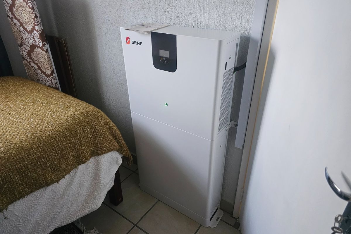 A bedroom featuring a wall-mounted SRNE solar inverter unit and tiled flooring.