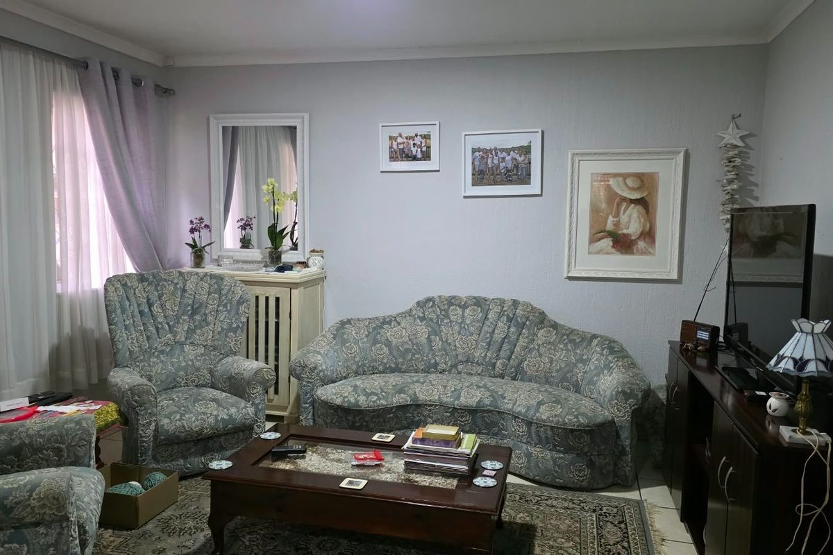 A comfortable living room featuring tiled flooring, coved cornicing, and large windows with curtain tracks, offering a functional and well-maintained space.