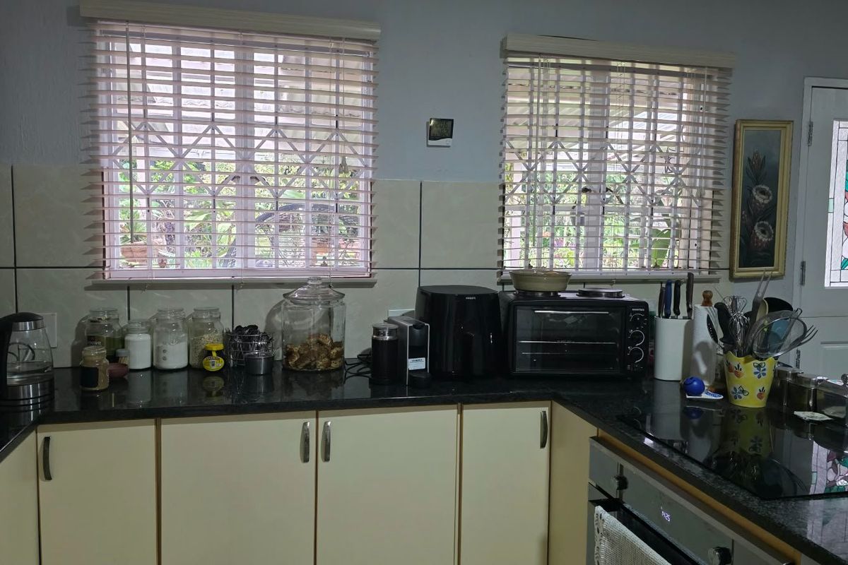 Functional kitchen featuring granite countertops, built-in oven, ceramic hob, tiled backsplash, and ample cabinetry, complemented by natural light through window blinds.