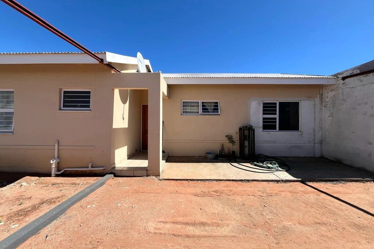 Rear view of the property featuring a concrete patio area, aluminium window frames, and unfinished exterior wall sections with an unlandscaped yard.