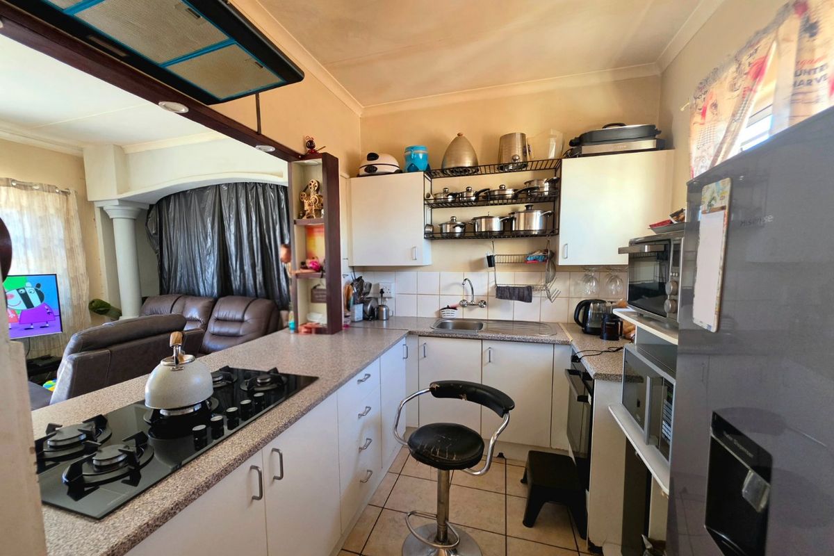 Compact kitchen featuring white cabinetry, a gas hob with extractor fan, tiled backsplash, and a breakfast counter overlooking the living area.