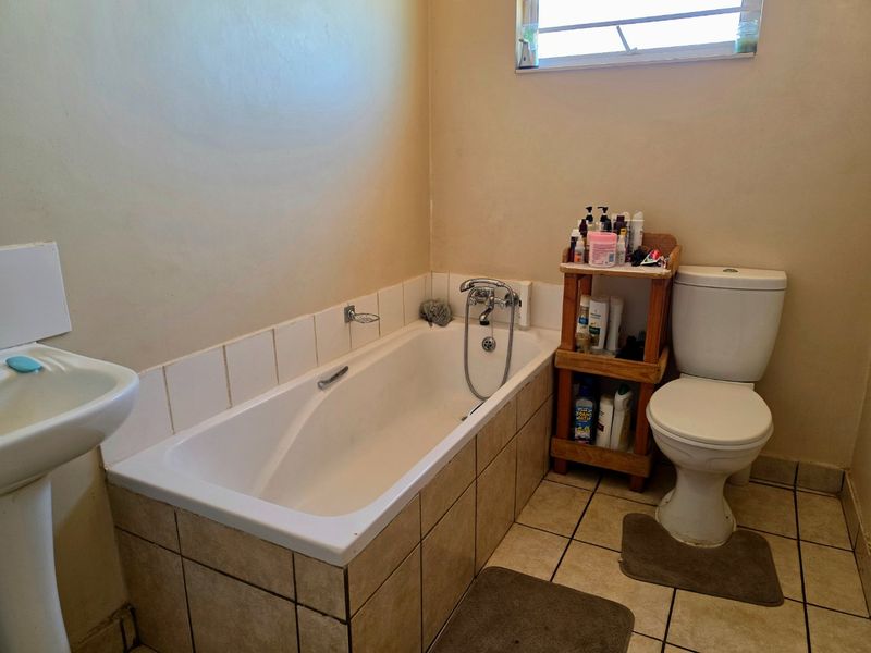 A functional bathroom featuring a bathtub with tiled surround, pedestal basin, and toilet, finished with tiled flooring and a louver window.
