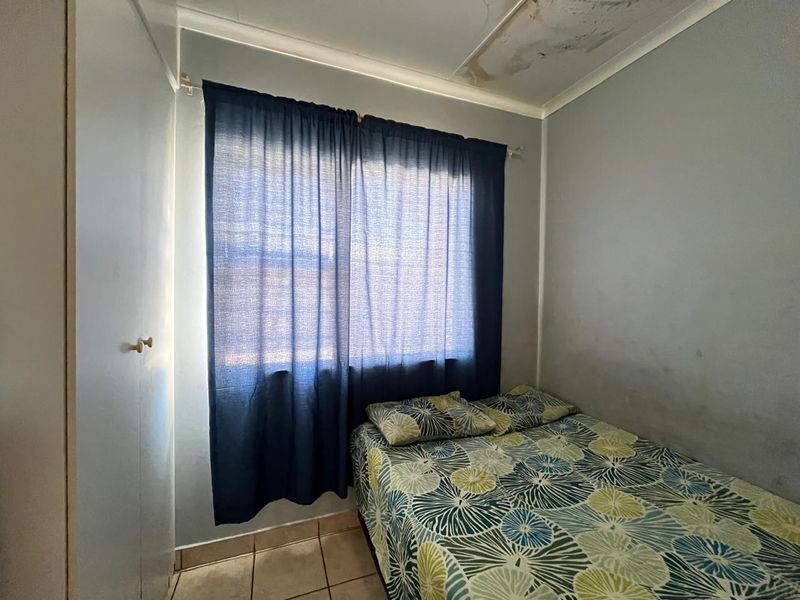 A compact bedroom featuring tiled flooring and a built-in cupboard, showing visible signs of ceiling water damage requiring maintenance.