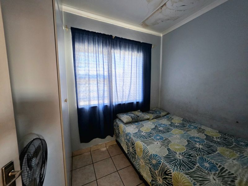 A compact bedroom featuring tiled flooring and a built-in cupboard, currently showing signs of ceiling water damage and wall staining.