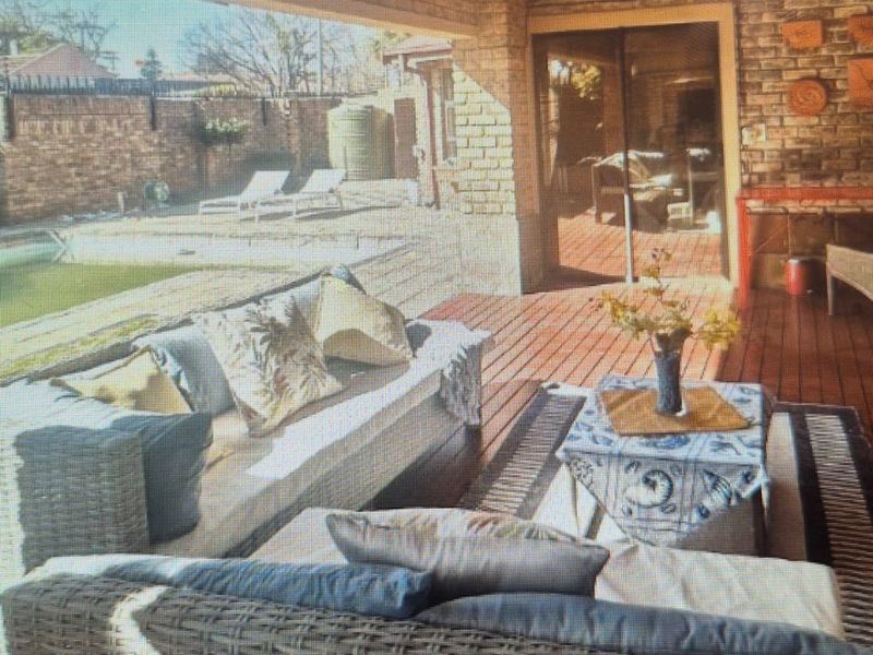 A covered outdoor patio featuring timber decking and exposed brick walls, providing a seamless transition to the garden and pool area.