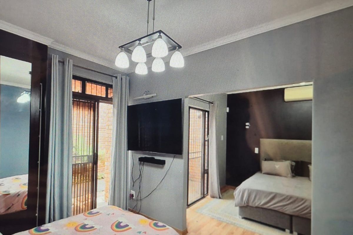 A bedroom featuring laminate flooring, coving, and sliding glass doors leading to an outdoor area, with an adjoining sleeping space and air conditioning.