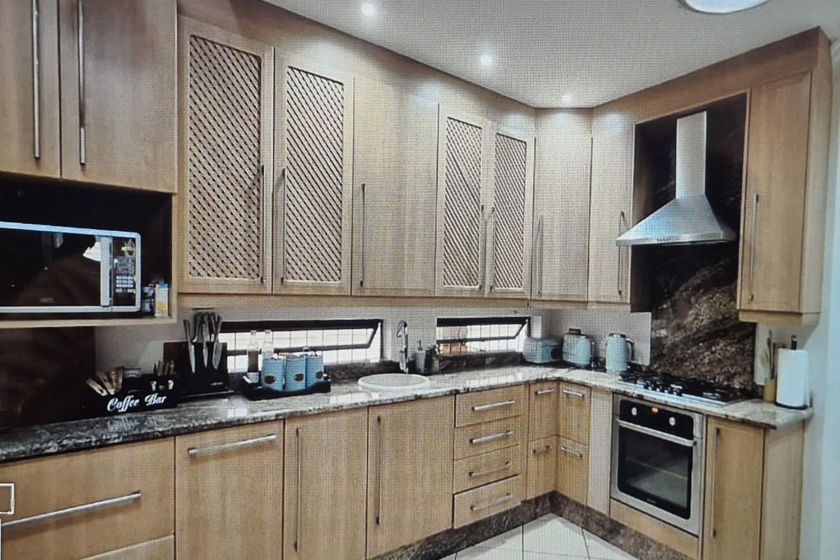 A well-appointed kitchen featuring light wood cabinetry, granite countertops, built-in appliances including an oven and hob, and modern recessed lighting.