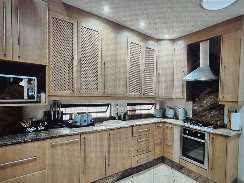 A well-appointed kitchen featuring light wood cabinetry, granite countertops, built-in appliances including an oven and hob, and modern recessed lighting.