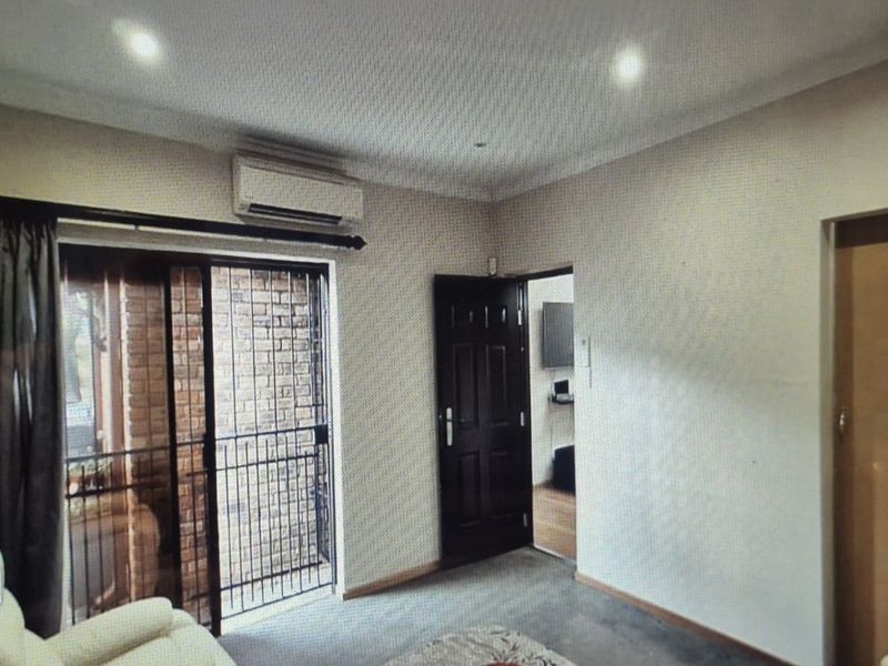 Living area featuring recessed downlights, a wall-mounted air conditioning unit, and a sliding glass door with a security gate leading to the exterior.