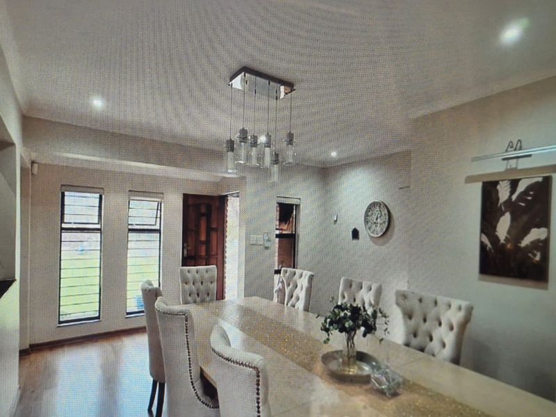 A well-lit dining room featuring laminate flooring, modern pendant lighting, and windows fitted with security bars.