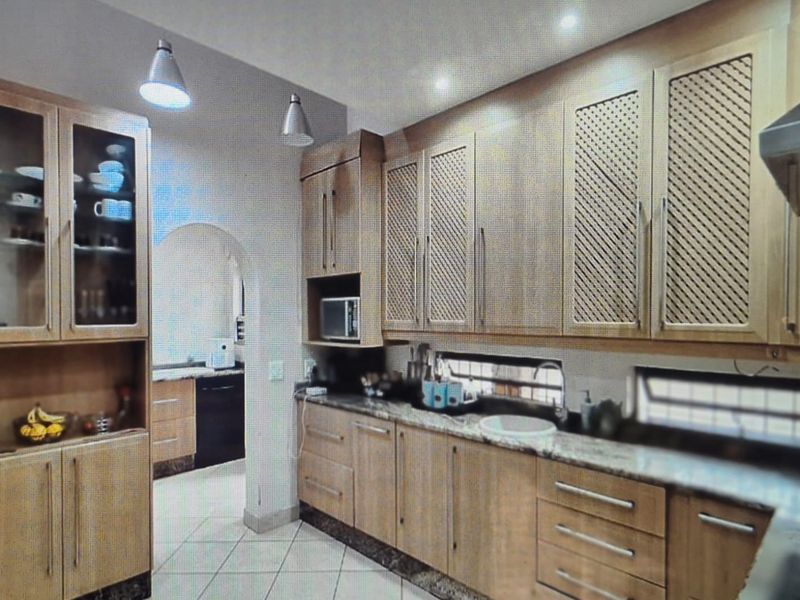 A functional kitchen featuring wooden cabinetry with lattice detailing, granite countertops, and an integrated microwave, with an adjacent scullery area visible through an archway.