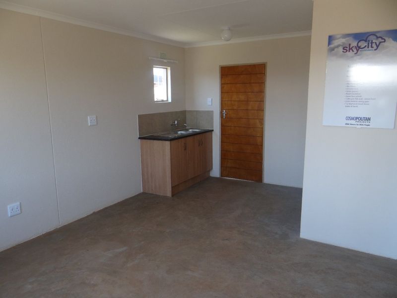 A compact, empty kitchen area featuring basic base cabinetry, a sink, and tiled splashback, suitable for a starter home or utility space.