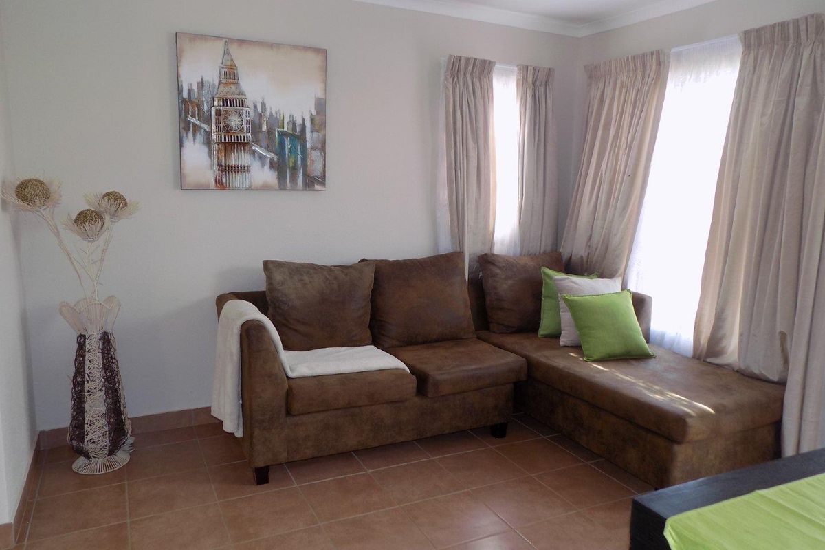 A living room area featuring neutral wall tones, tiled flooring, and natural light through window treatments.