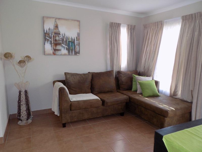 A living room area featuring neutral wall tones, tiled flooring, and natural light through window treatments.