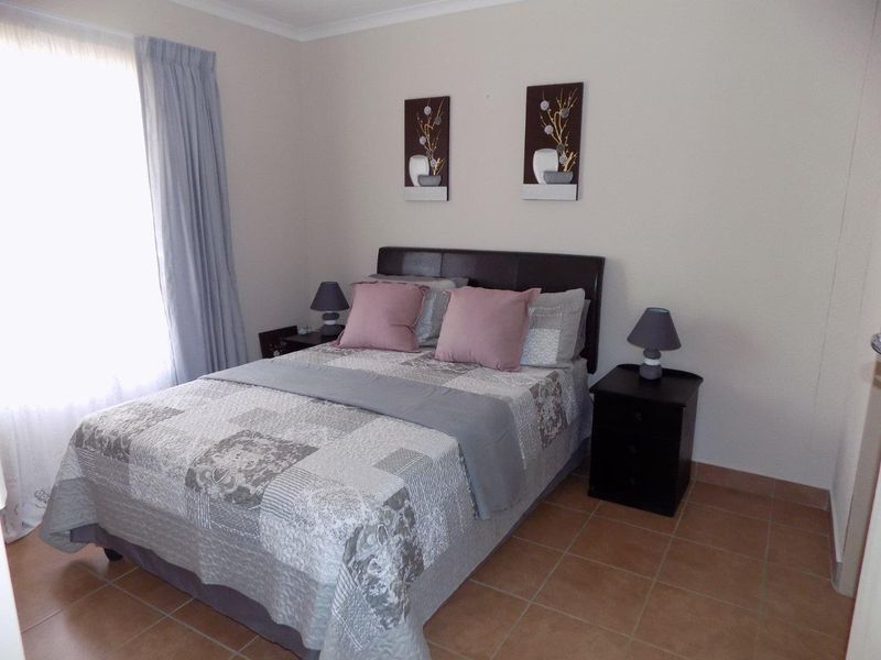 A well-maintained bedroom featuring neutral wall tones, tiled flooring, and a large window allowing for natural light.