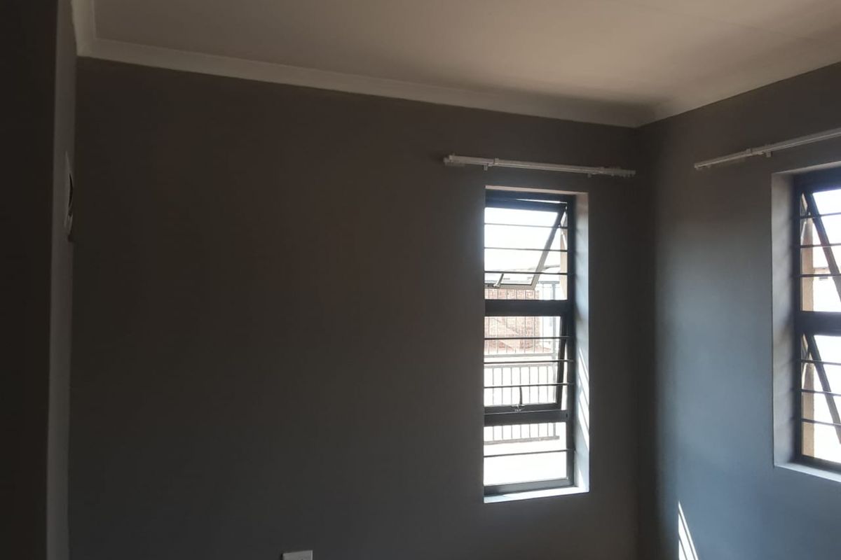 A clean, empty bedroom featuring grey painted walls, metal security bars on the windows, and installed curtain rails.