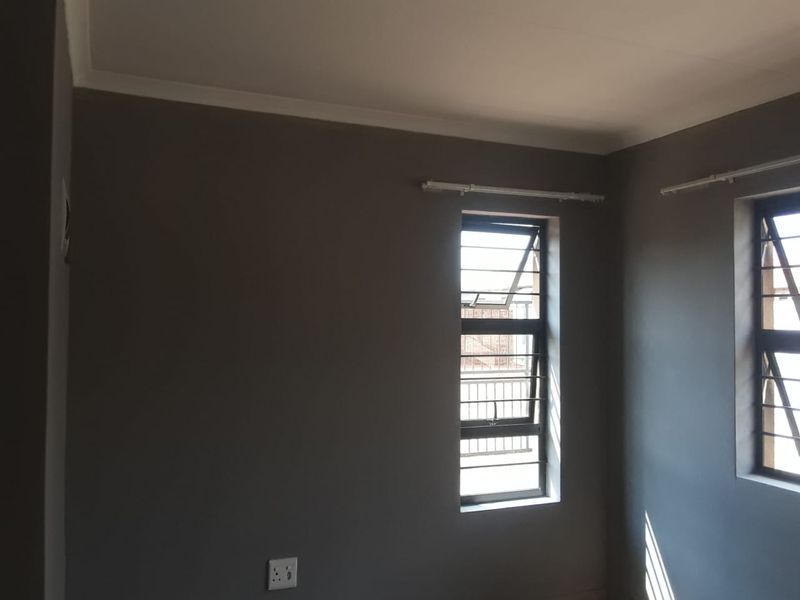 A clean, empty bedroom featuring grey painted walls, metal security bars on the windows, and installed curtain rails.