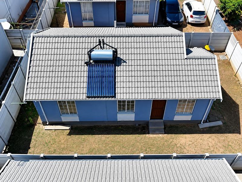 Aerial view of a residential property featuring a tiled roof with an installed solar water heating system and a fenced yard.