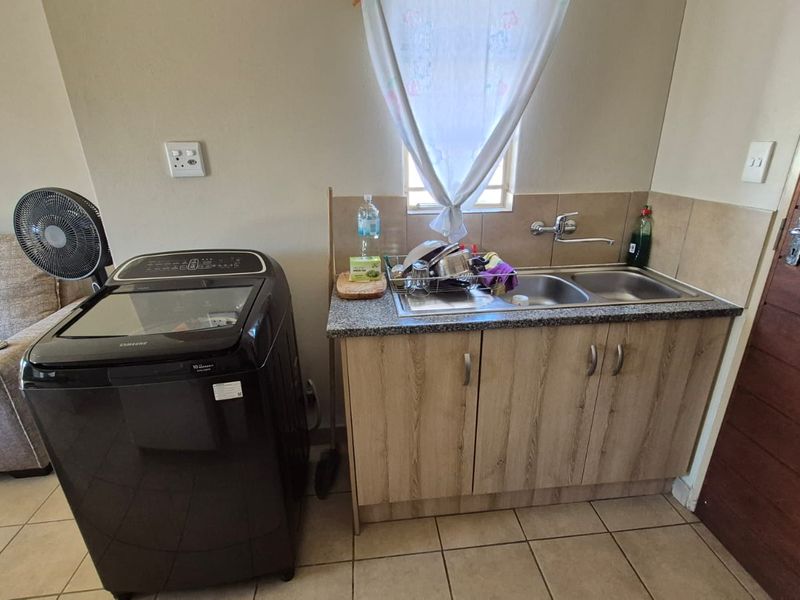 A functional laundry area featuring a double basin sink, granite countertop, and laminate cabinetry with tiled splashback and flooring.