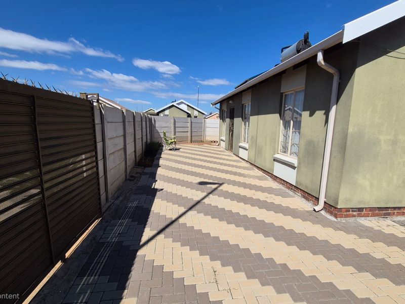 A paved rear exterior area featuring a precast concrete boundary wall, solar water heating system, and exterior wall finishes.