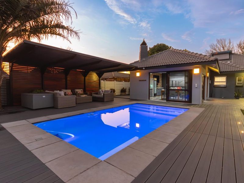 A well-maintained outdoor entertainment area featuring a swimming pool, composite decking, and a covered patio with integrated lighting and direct access to the home.