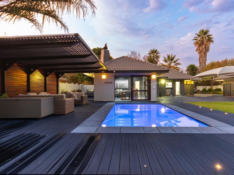 A beautifully maintained outdoor entertainment area featuring a swimming pool, modern timber decking, and a covered patio space with integrated lighting.