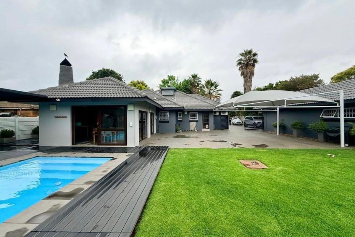 Spacious rear exterior featuring a swimming pool with composite decking, a paved driveway, shade sail, and an outdoor fireplace.